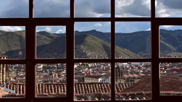 A view through a window with multiple panes, each displaying a different section of a cityscape with hills and buildings. - Kuska Guest House (Cusco)