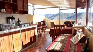 A kitchen with a large island, wooden cabinets, and a view of mountains through large windows. - Kuska Guest House (Cusco)