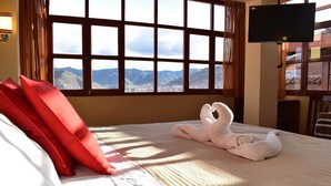 A hotel room with a large window offering a mountain view, a bed with red pillows, and a flat-screen TV on a stand. - Kuska Guest House (Cusco)