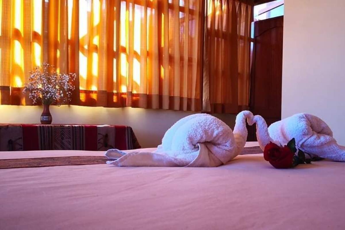 Una cama con dos toallas con forma de cisne y una rosa roja.