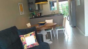 A living room with a dark sofa, a wooden dining table, and a kitchen in the background.