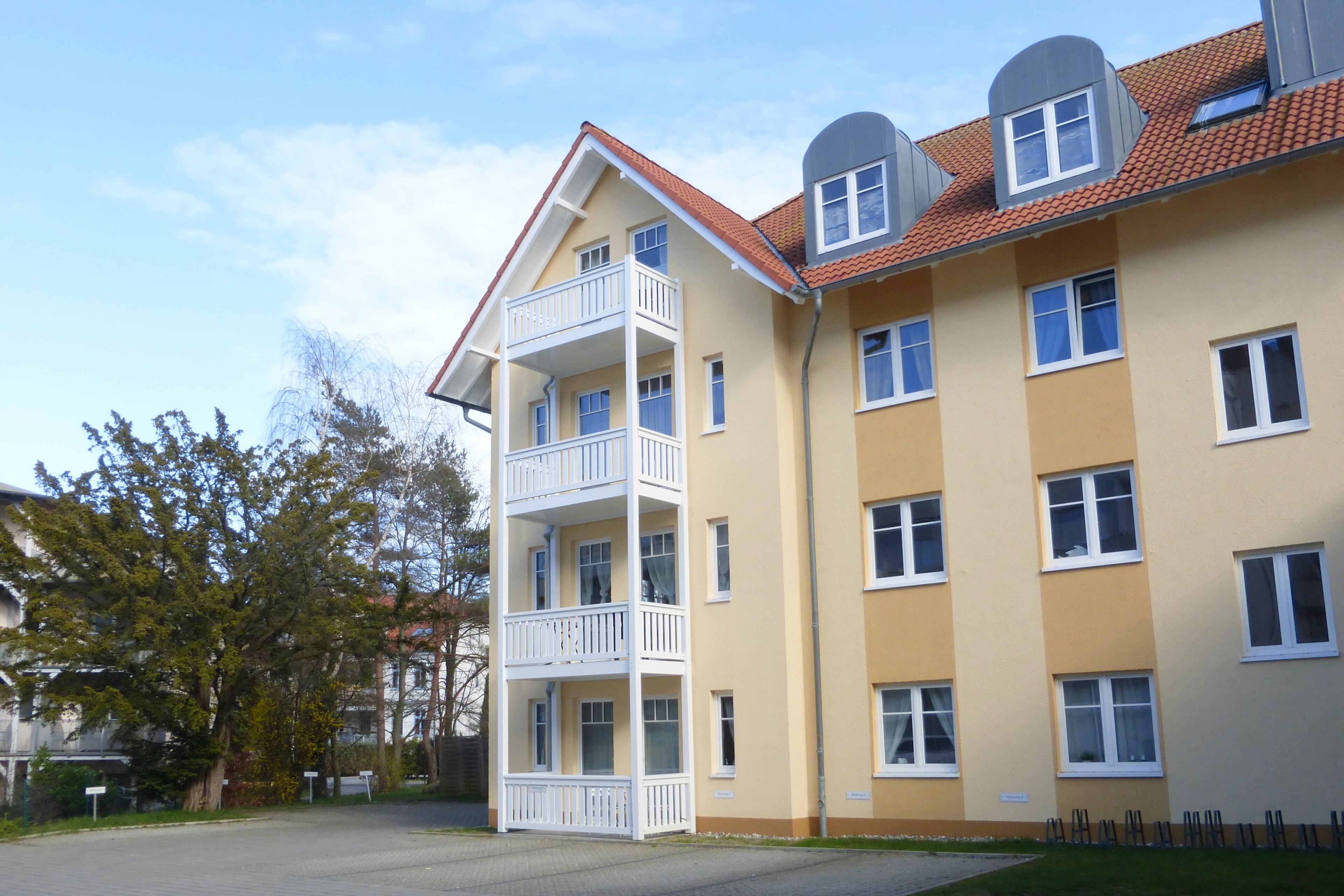 Ein mehrgeschossiges Wohngebäude mit Balkonen und einem roten Ziegeldach.