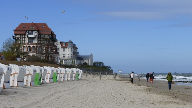 A beach with a row of white beach chairs, a large building with a red roof, and a clear blue sky. - Central, 300m from the beach, Apartment Strandschlösschen II, family-friendly (Kühlungsborn)