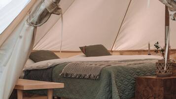 Een tent met een bed, een tafel en een bijzettafeltje van hout.