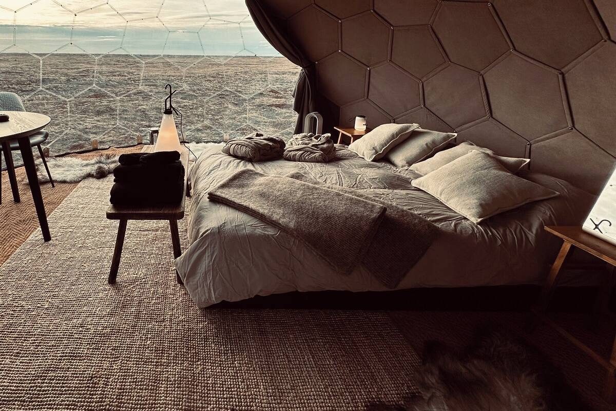 Un dormitorio moderno con techo hexagonal, una cama con almohadas, una mesita y vistas al paisaje.