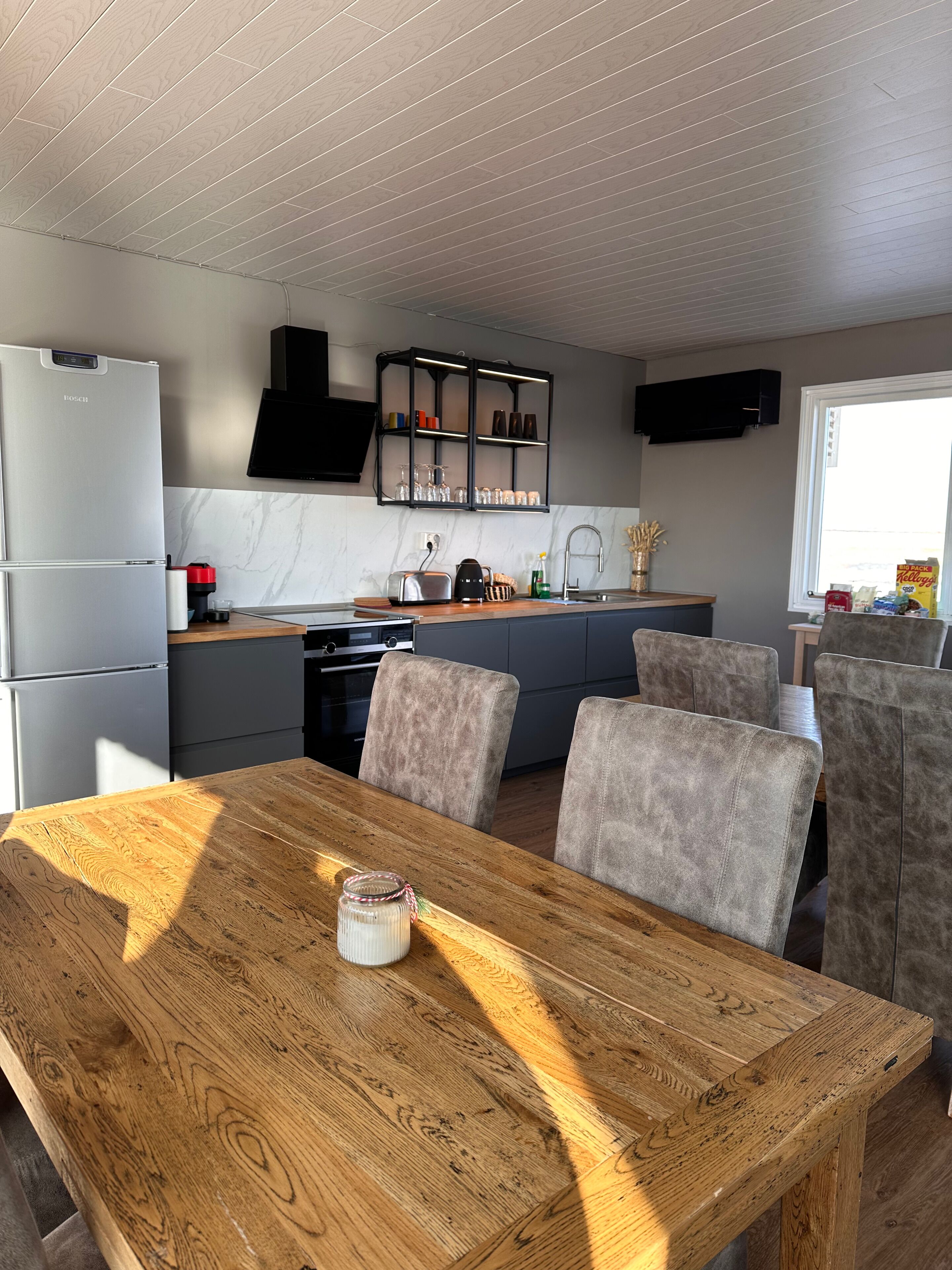 A modern kitchen with a wooden dining table, grey cabinets, and a black range hood.