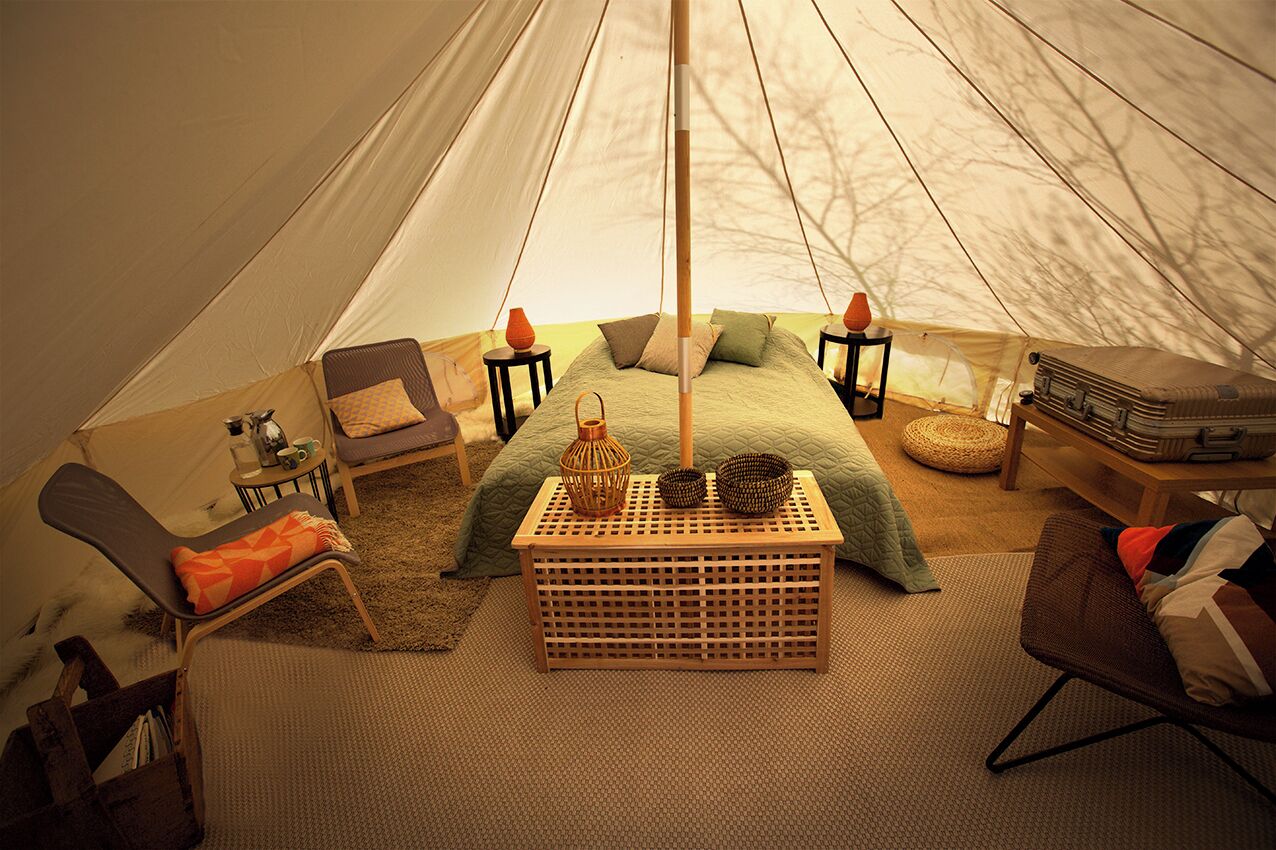 Interior de uma tenda com uma cama, assentos, uma mesa e um suporte para bagagem.