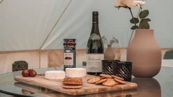 Una mesa con una botella de vino, un tarro de mermelada, un florero con una flor y varios alimentos.