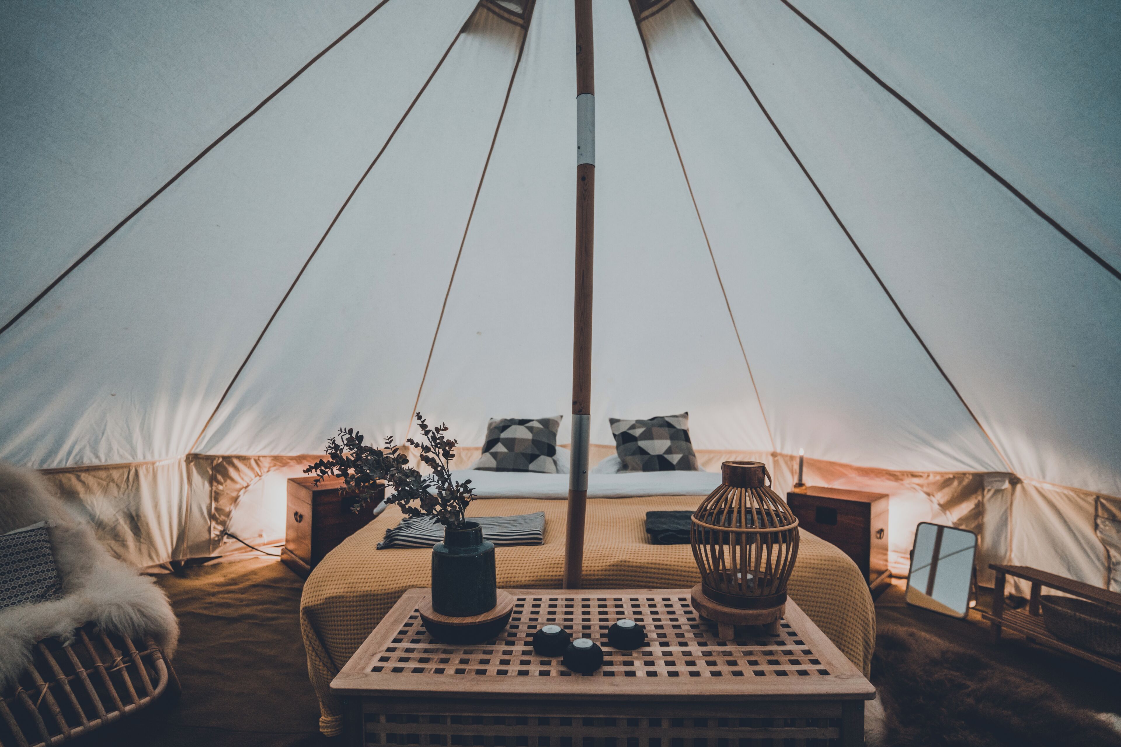 A tent interior with a bed, pillows, a table with a vase and candles, and a hanging light fixture.