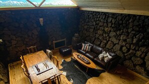 Una habitació acollidora amb un paviment de fusta, parets de pedra, una llar de pedra i un sofà de cuir, a més d'una taula de dinar amb cadires.