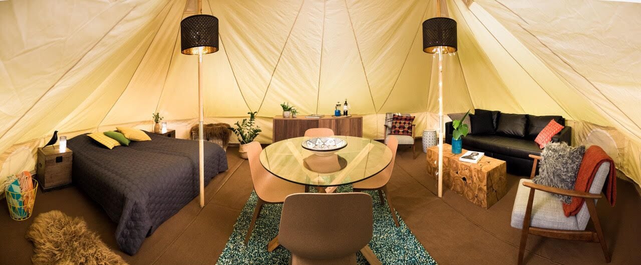 Interior de una tienda de campaña con cama, mesa redonda y zona de estar.