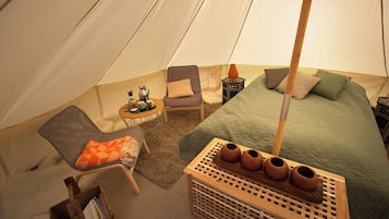 Interior de una tienda de campaña con una cama, dos sillas, una mesita y una cesta de cerámica.