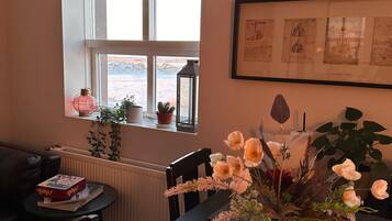 A dining area with a table, chairs, a vase with flowers, a window with a view, and framed pictures on the wall.