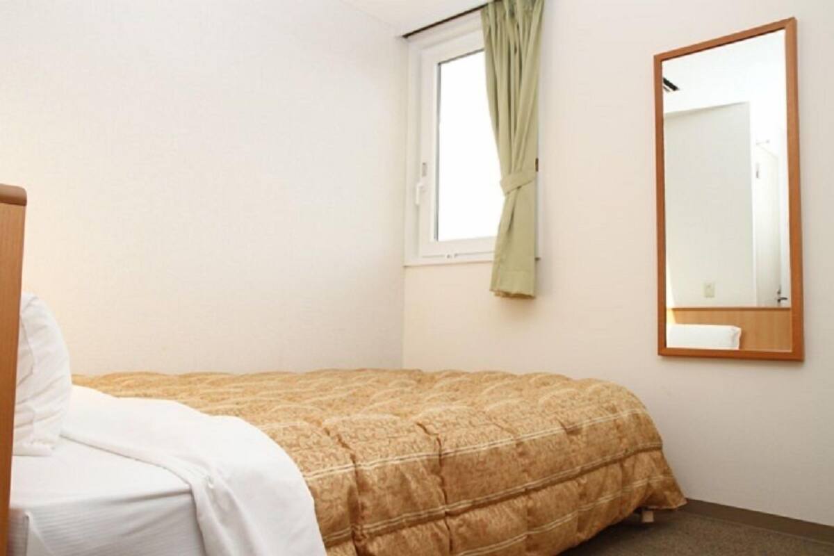 A bedroom with a bed, a window with curtains, and a mirror on the wall.