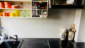 Keittiössä on musta työtaso, pesuallas ja liesi. Työtason yläpuolella on hyllyjä, joilla säilytetään erilaisia keittiötarvikkeita.