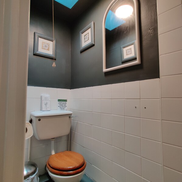 Ein kleines Badezimmer mit Toilette, Waschbecken und Spiegel. An den Wänden hängen Bilder in Rahmen und über dem Waschbecken befindet sich ein Schild.