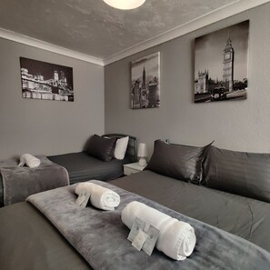 Habitación de hotel con dos camas, ropa de cama gris y tres cuadros con vistas de monumentos de Londres.