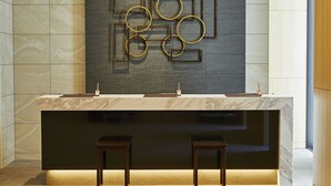 Een moderne receptiebalie met een marmeren blad, twee houten krukken en een wanddecoratie met geometrische vormen.