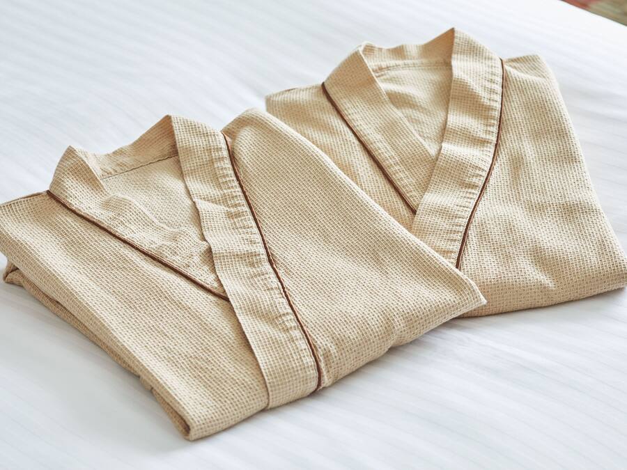 A neatly folded beige shirt on a white bed.