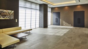 Een ruime lobby met een gele bank, een zitbankje en een betegelde vloer.