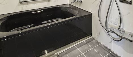 A modern bathroom with a black bathtub, a handheld showerhead, and a wall-mounted mirror.