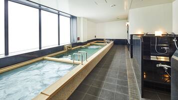 A long indoor swimming pool with clear water, adjacent to a sauna area with black tiles and a glass partition.