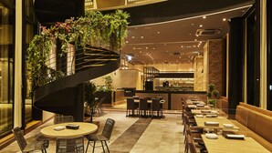 Een modern restaurant met een spiraaltrap, meerdere eettafels en een bar.