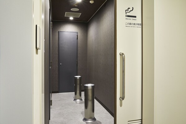 Un pasillo con una puerta al final, un letrero que indica una zona para fumadores y dos contenedores cilíndricos de basura.