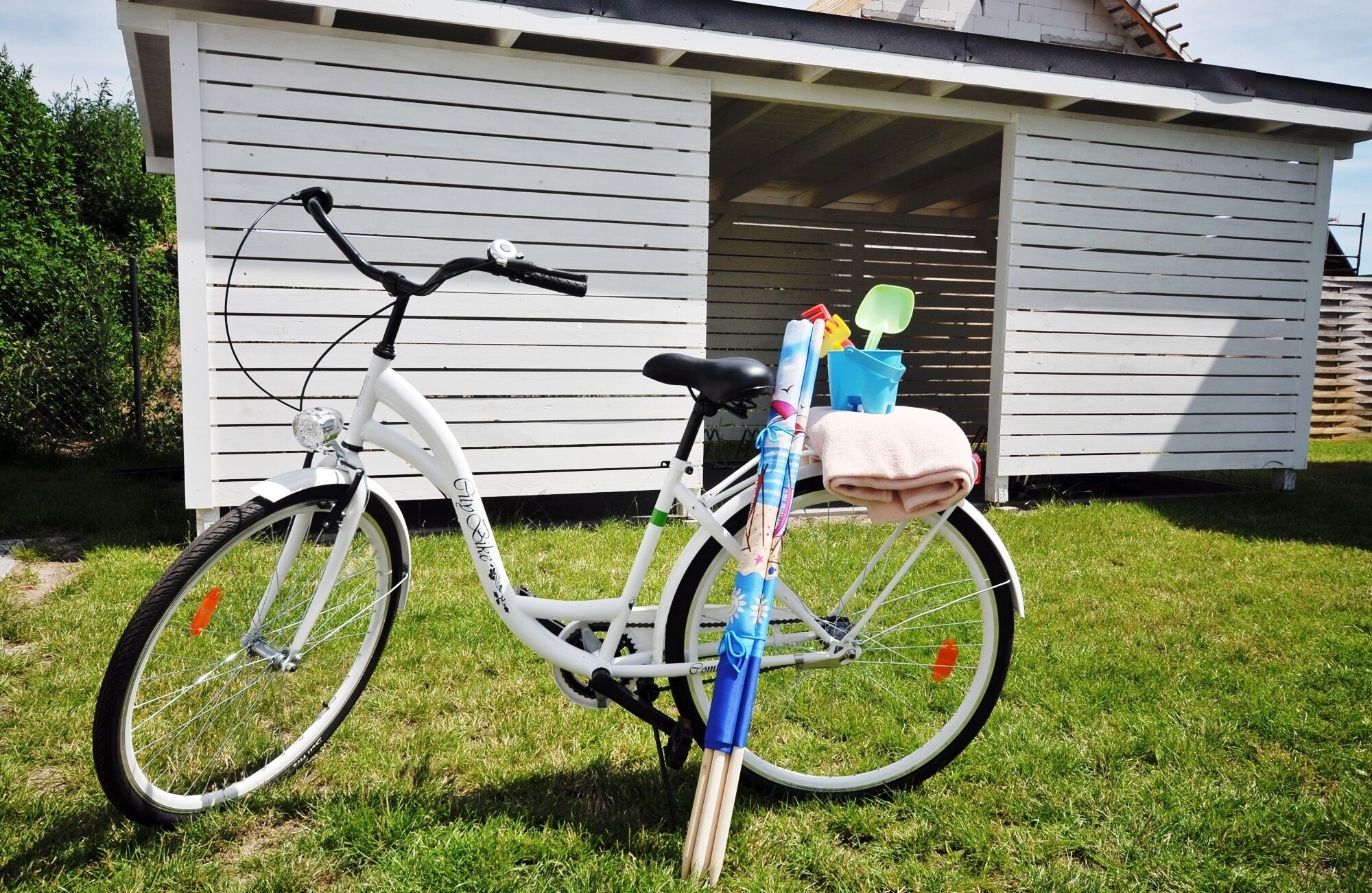 A white bicycle parked on grass in front of a white building with a garage door.