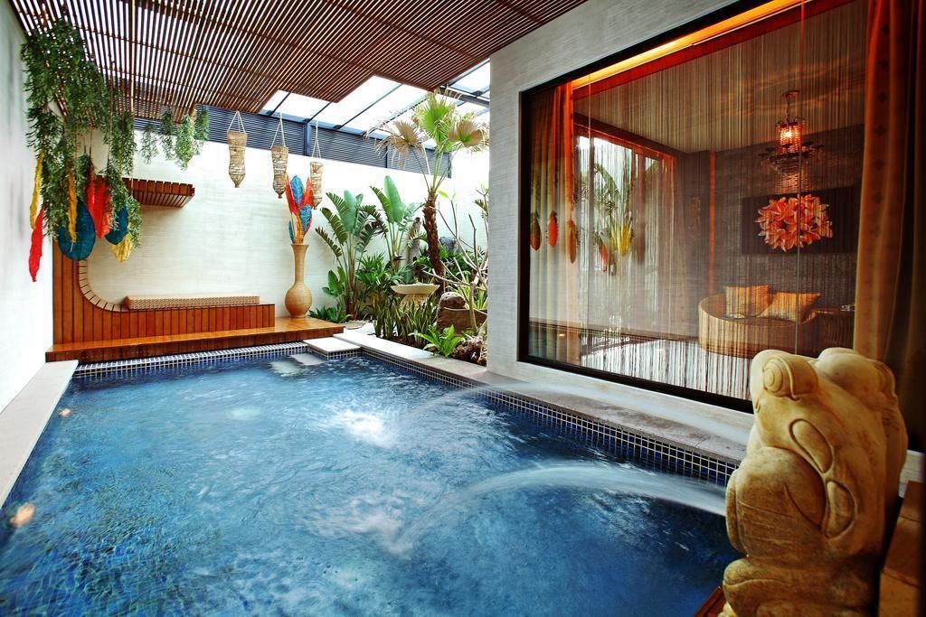 Uma área interna de piscina moderna, com espaço de estar, uma janela grande com cortinas e diversas plantas.