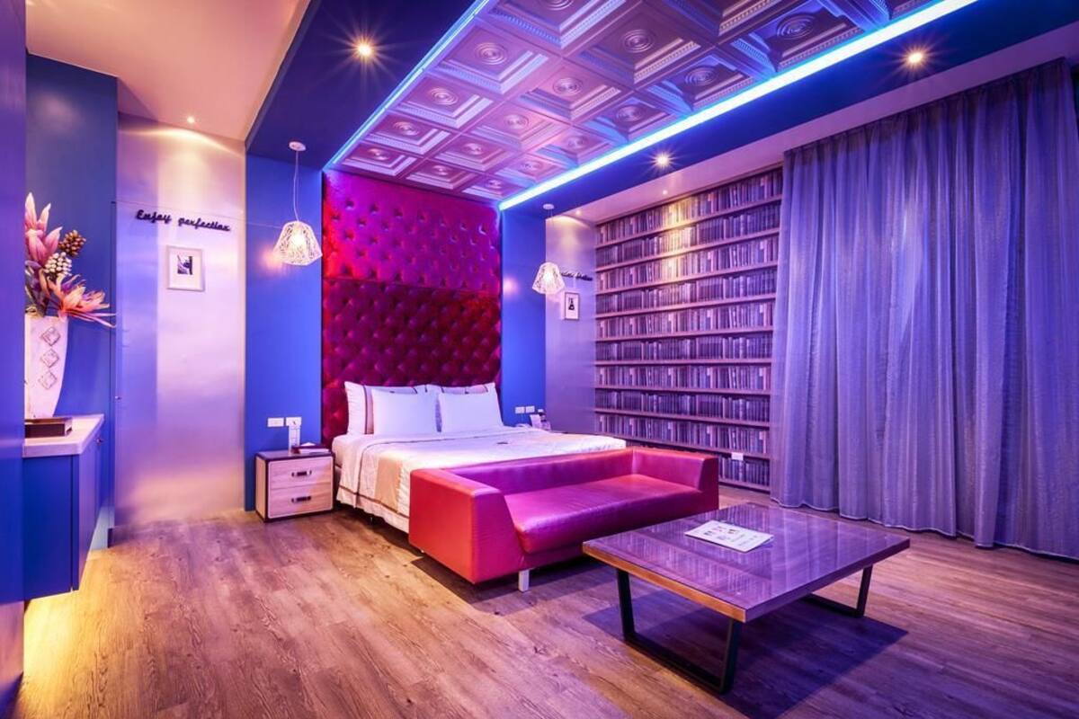 A modern bedroom with a large bed, a red sofa, a coffee table, and a bookshelf.