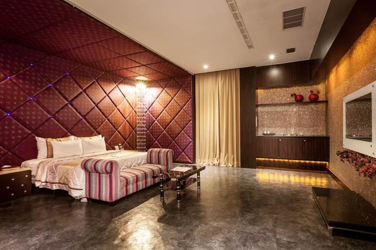A modern bedroom with a tufted headboard, a bed with striped bedding, a small sofa, a nightstand, and a decorative wall with a shelf.