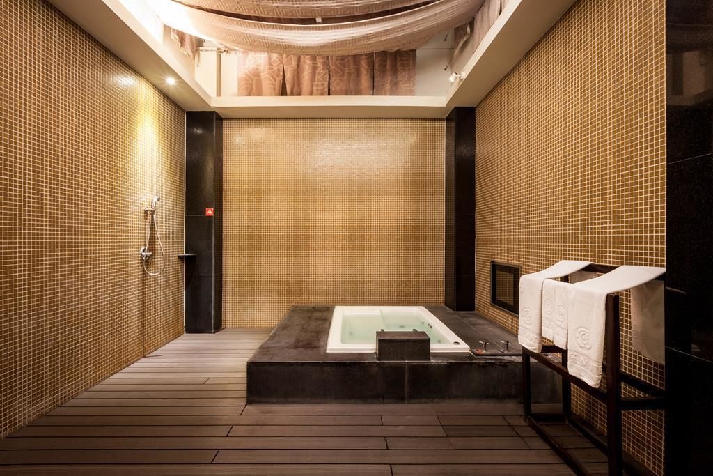 A modern spa room with a large bathtub, wooden flooring, and tiled walls.