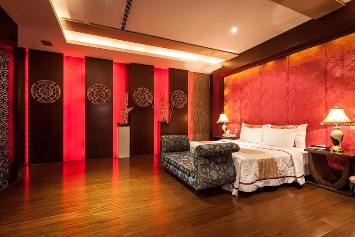 A hotel room with a wooden floor, a sofa, a bed, and decorative wall panels.