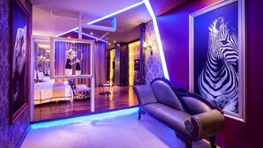 Una habitación de hotel moderna con una cama, un sofá, una mesita y un cuadro grande de cebra en la pared.