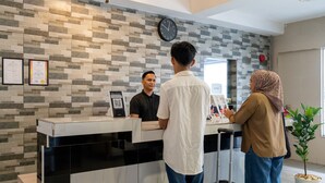A reception desk with a tiled wall, a clock, framed certificates, and a potted plant. - Pertama Lodge (Tawau)