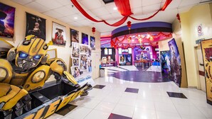 A cinema lobby with a yellow car ride, movie posters, and red decorations. - Pertama Lodge (Tawau)