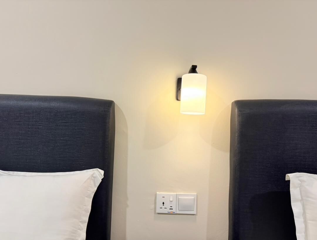 Ett hotellrum med två sängar, en väggmonterad lampa och ett eluttag.