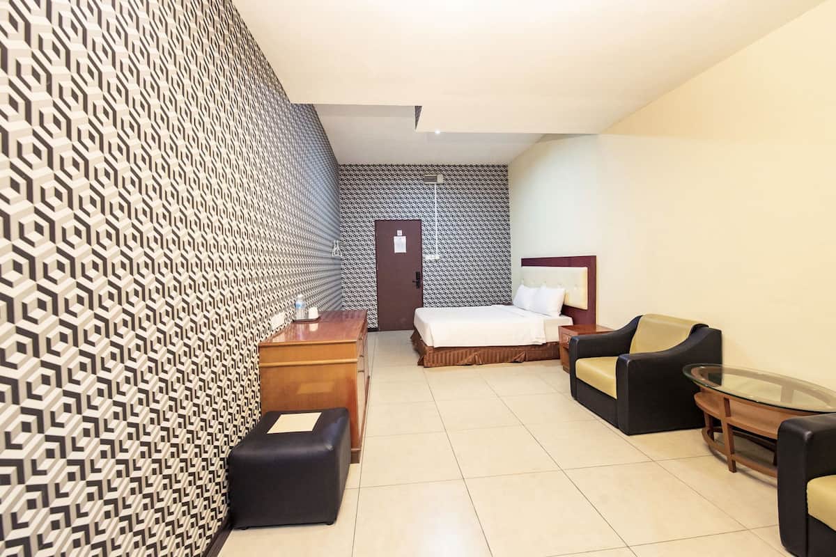 A hotel room with a patterned wall, a bed, a sofa, a desk, and a small table.