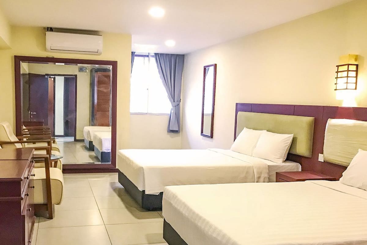 A hotel room with two beds, a desk, a chair, a mirror, and a window with curtains.