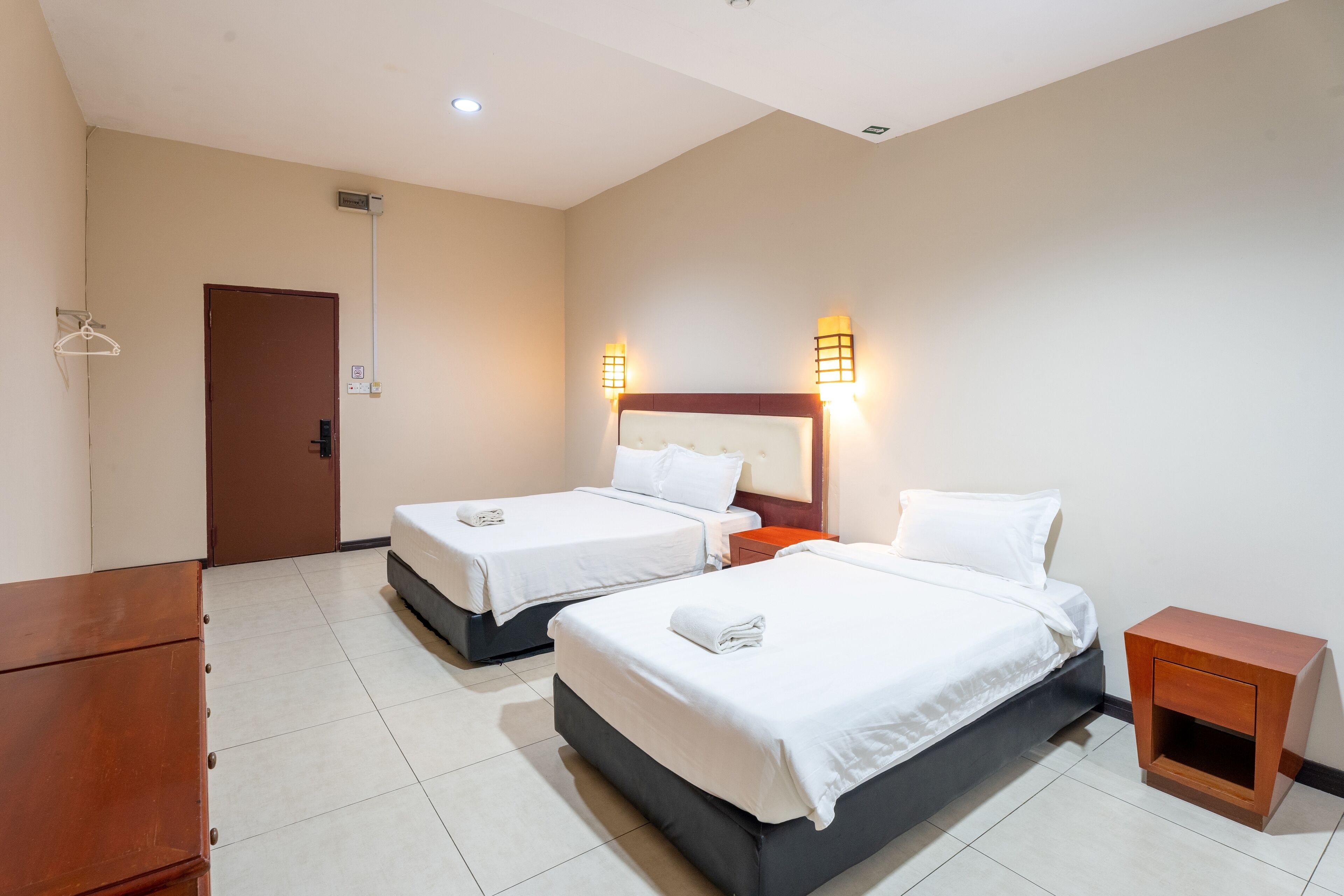 A hotel room with two beds, a wooden dresser, and a small nightstand.