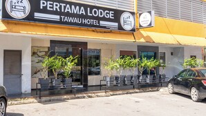 A hotel named Pertama Lodge with a signboard, outdoor seating, and a parked car. - Pertama Lodge (Tawau)