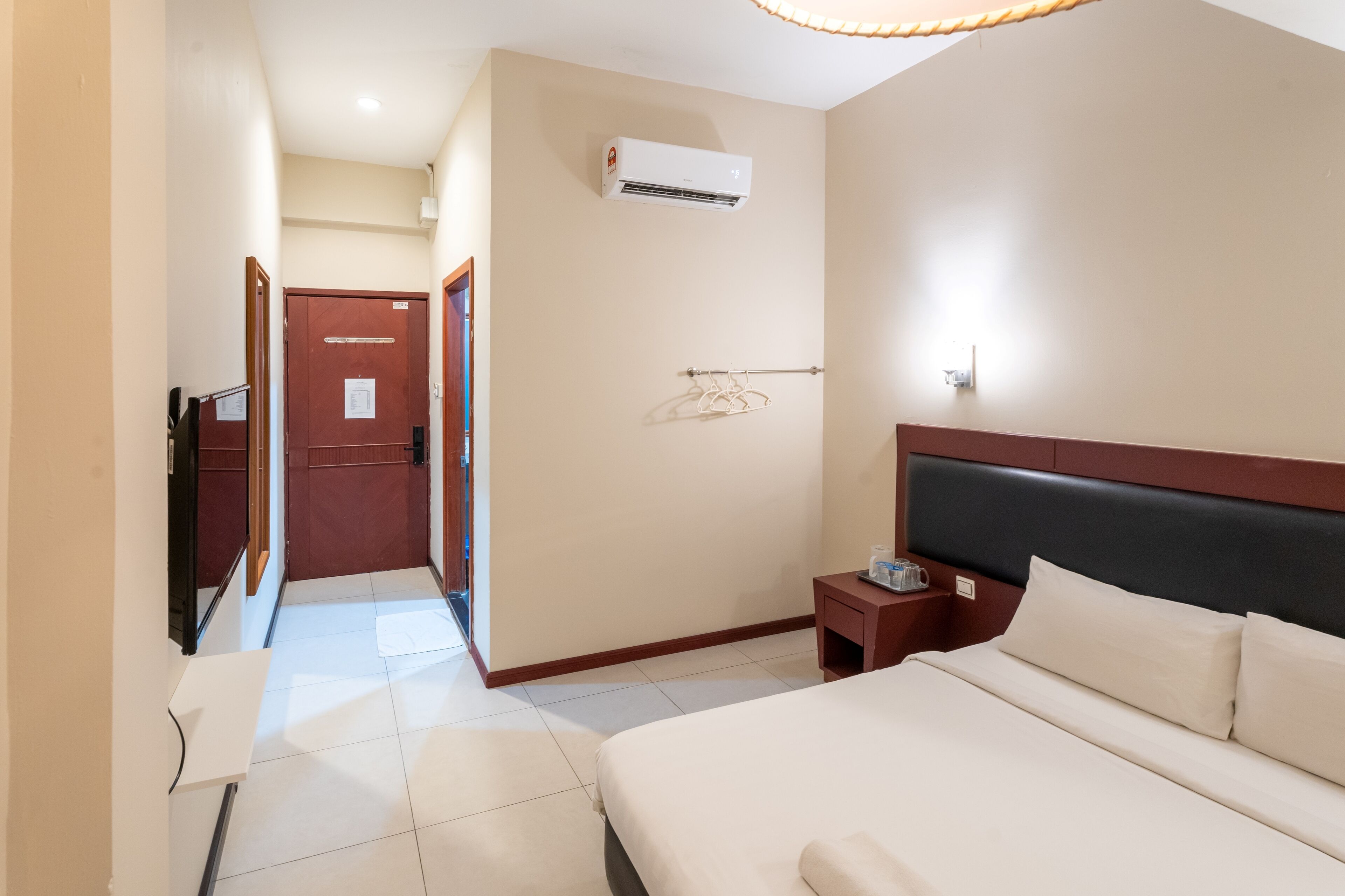 Habitación de hotel con cama, mesita de noche, televisión, aire acondicionado y puerta que da a otra habitación.