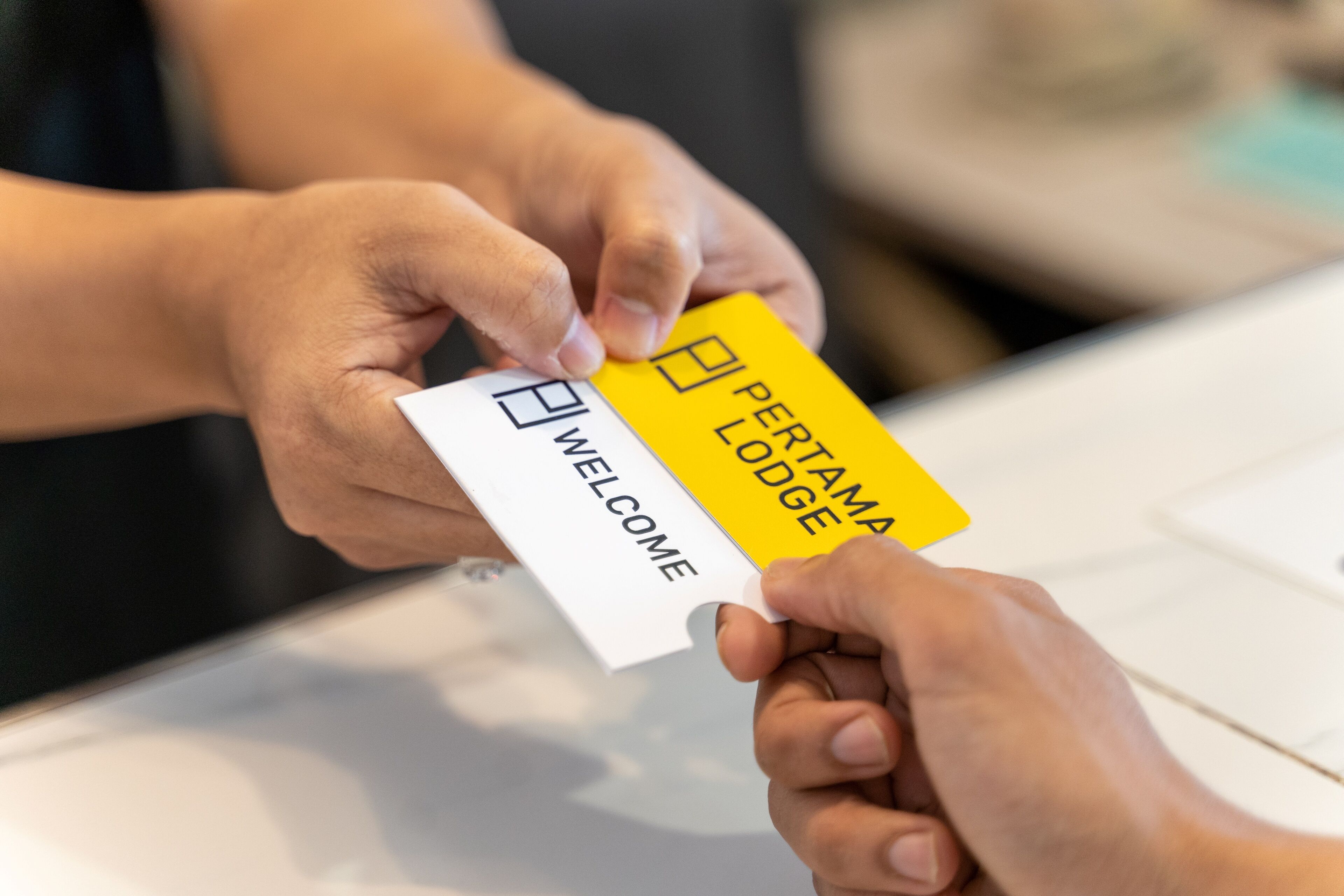 Eine Person übergibt eine gelbe Karte mit der Aufschrift 'PERFORMA LODGE' und eine weiße Karte mit 'WELCOME' an eine andere Person.