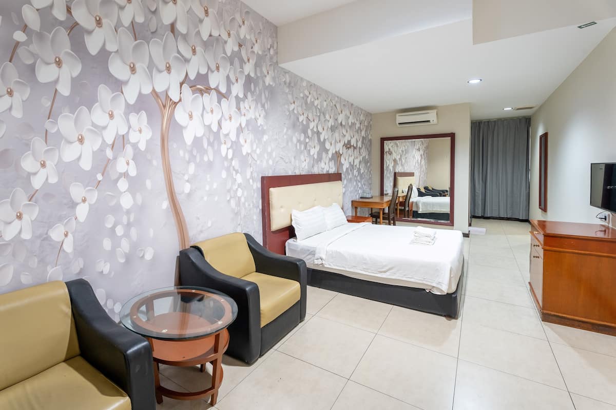 A hotel room with a bed, a sofa, a glass table, and a wall with a floral pattern.