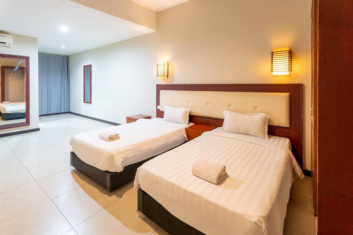 A hotel room with two beds, a mirror, and two wall-mounted lights.