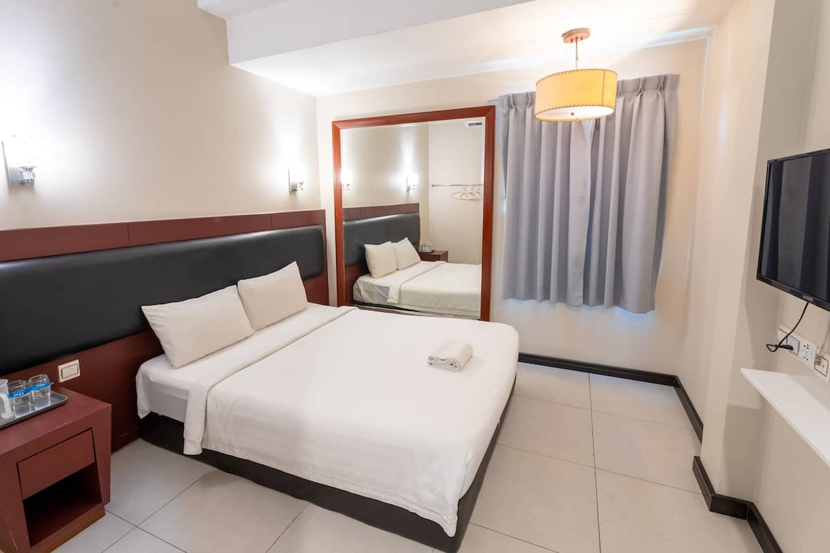 A hotel room with a bed, bedside table, TV, and a mirror.