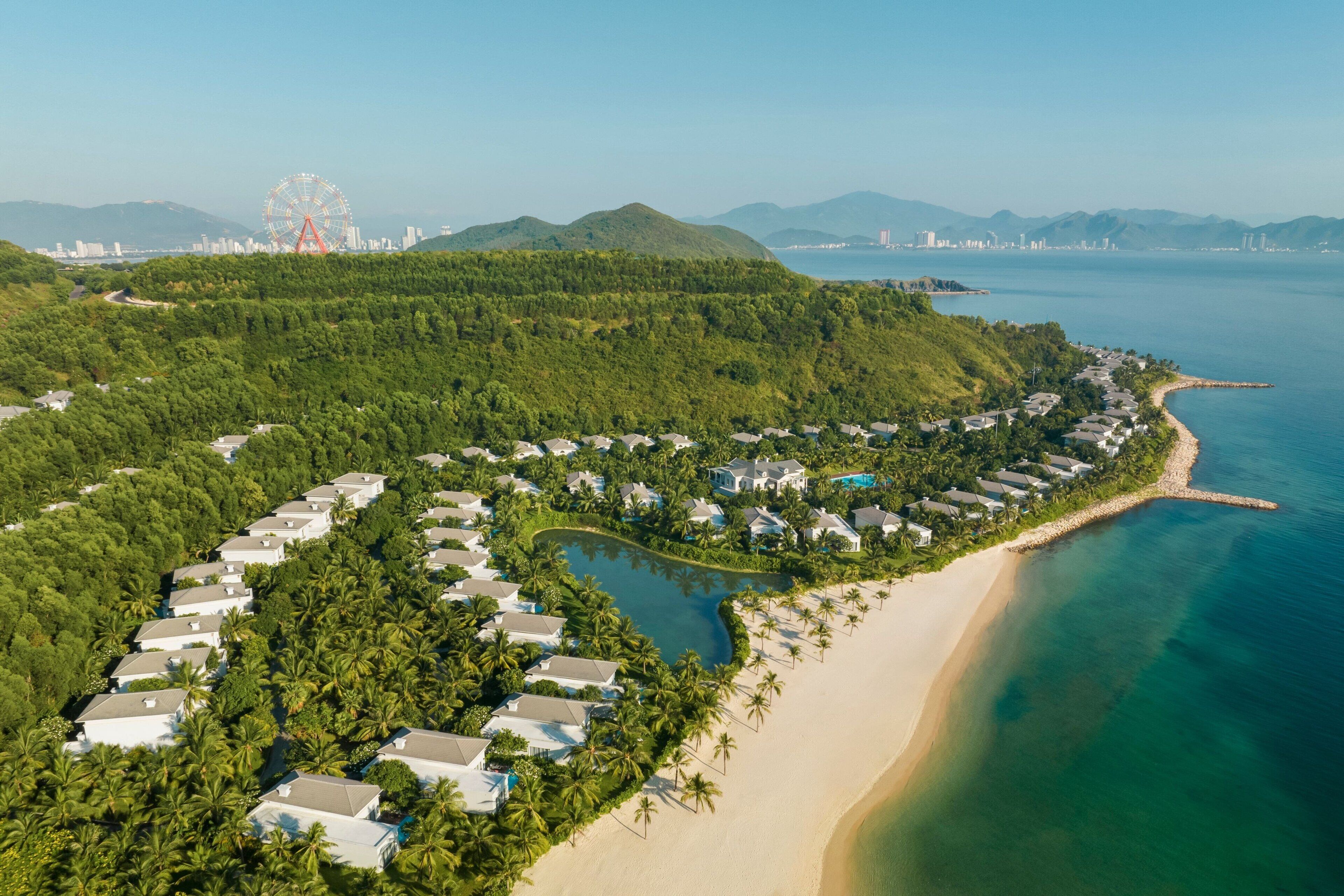 An aerial view of a coastal resort with villas, a beach, and a large body of water.
