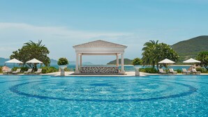 Une piscine avec des chaises longues et des parasols, un belvédère et une vue sur la mer et les collines.