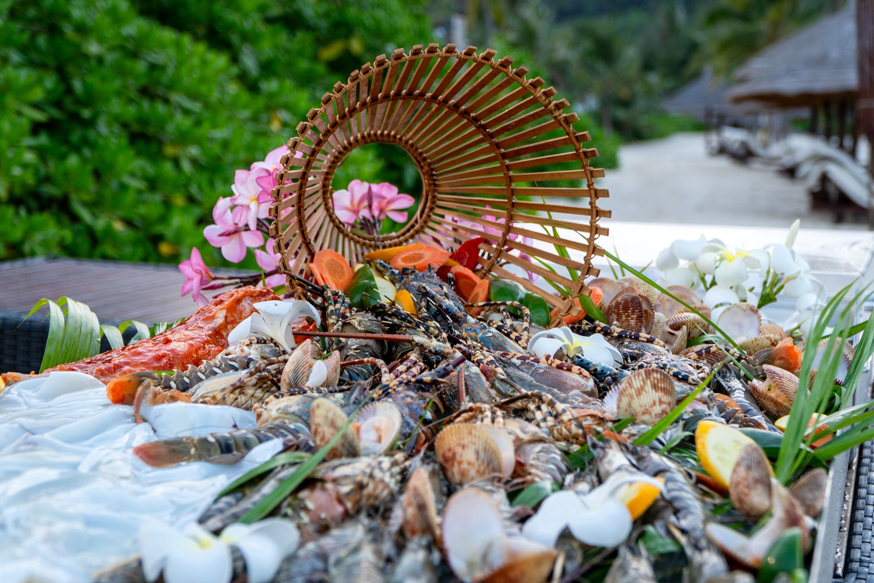 A tropical beach setting with a variety of seashells and flowers arranged on a table, surrounded by lush greenery.